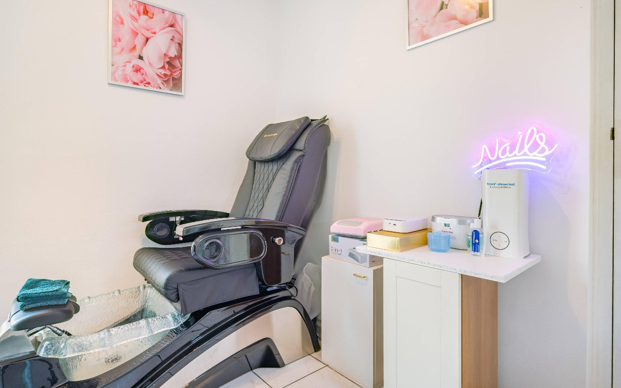 Zwarte pedicurestoel met voetbad en een neonbord Nails